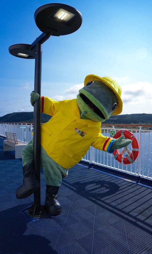 A mascot of a fish in yellow rain jacket and matching hat swings around a light post on a ferry.